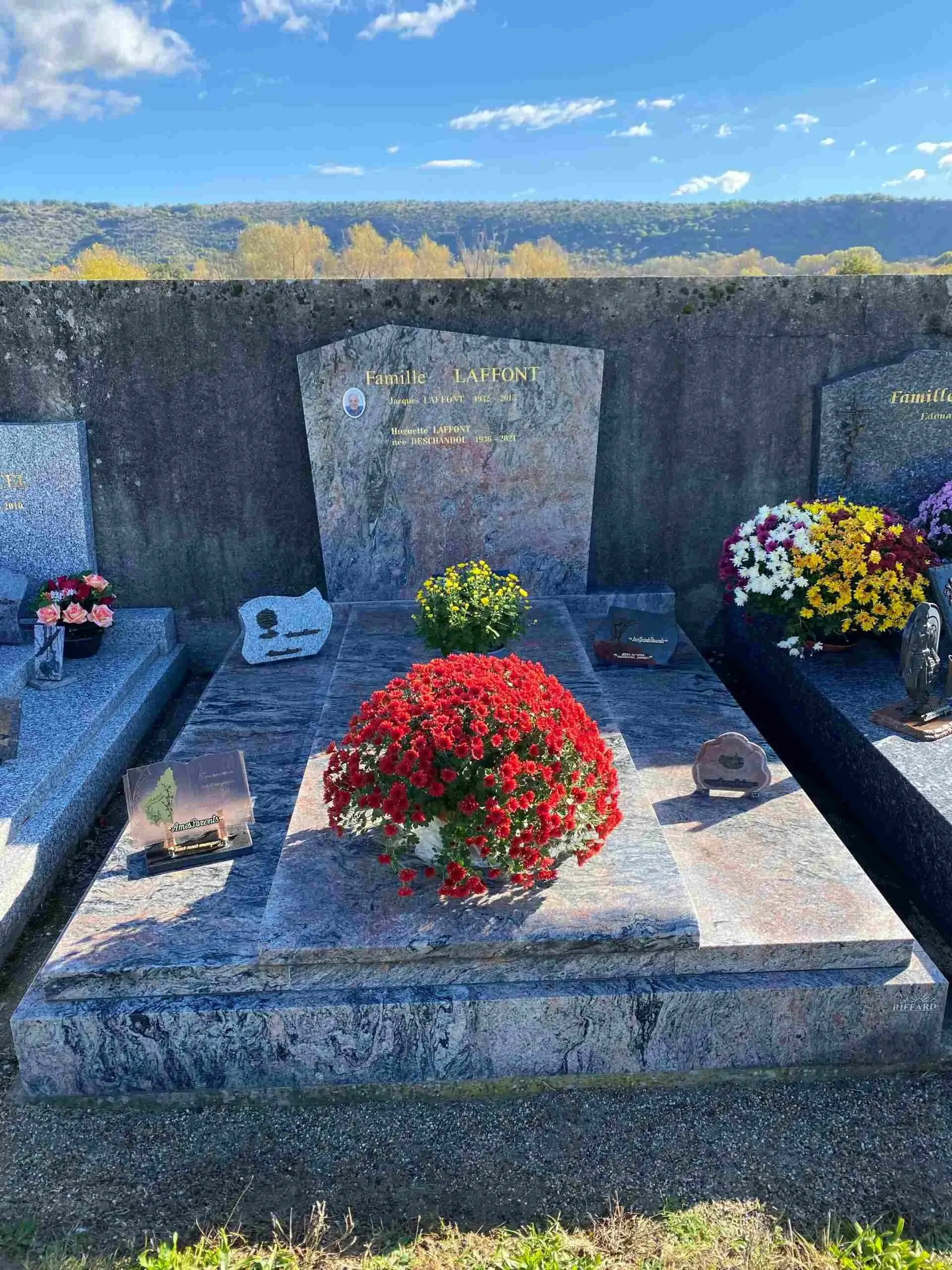 Sépulture en granit rose et veiné ornée d'un grand chrysanthème rouge.
