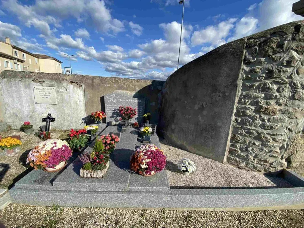 Monument funéraire en granit gris garni de pots de fleurs colorés au cimetière.