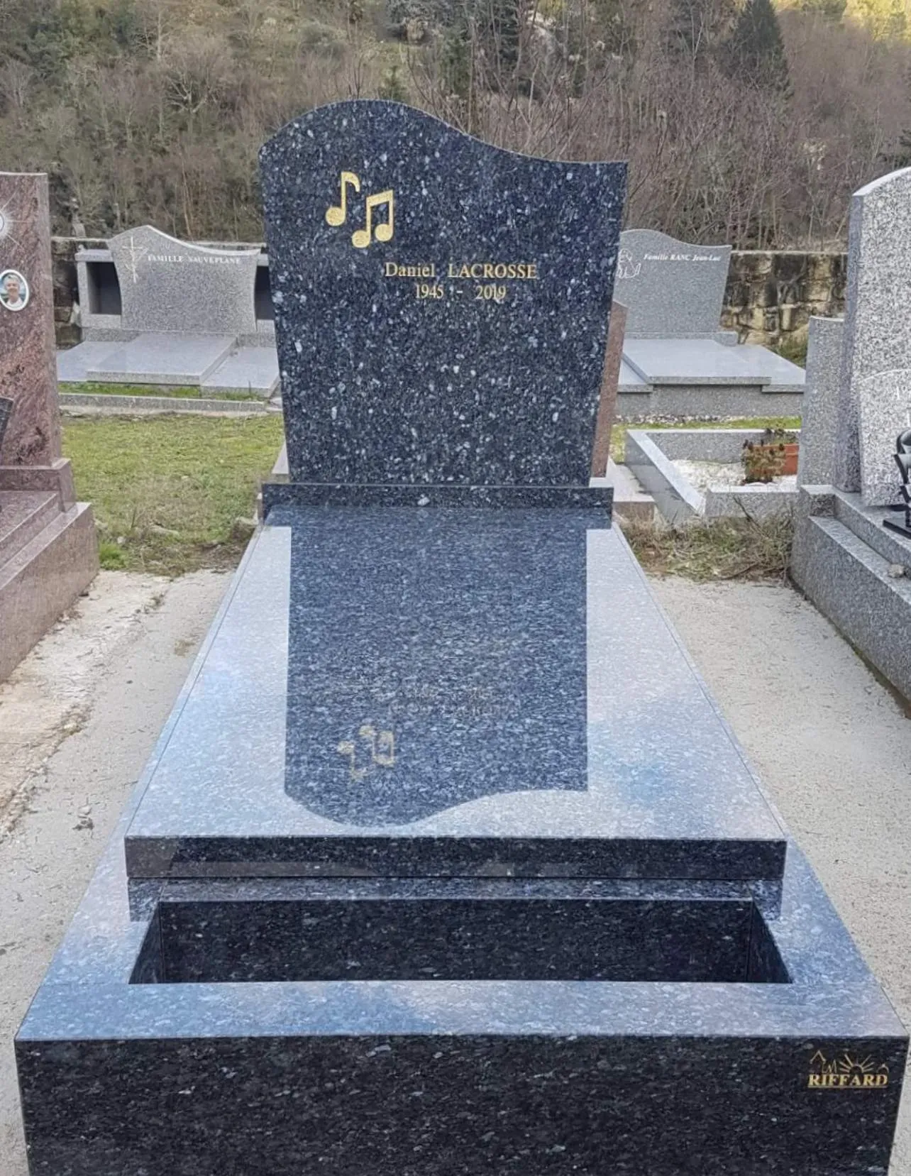 Monument funéraire en granit bleu nuit gravé de notes de musique dorées.
