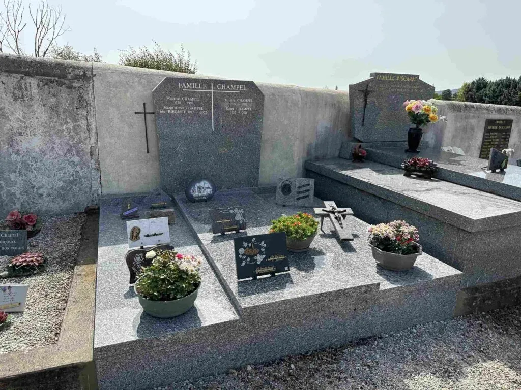 Sépulture familiale en granit gris ornée de poteries florales et plaques du souvenir.