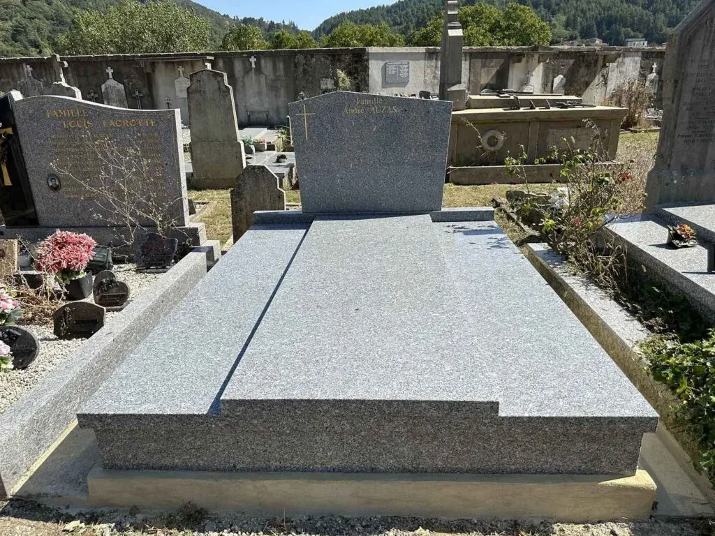Tombe en granit gris avec stèle classique et croix dorée au cimetière.