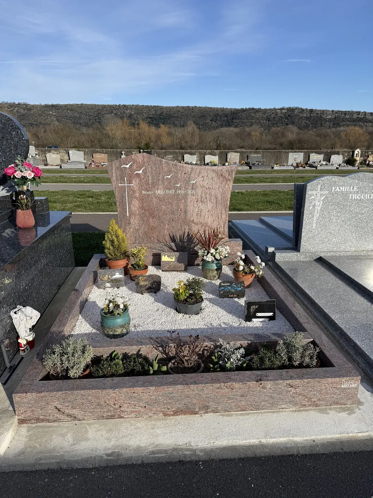 Sépulture paysagée en granit rose avec jardinière intégrée et gravures d'oiseaux.