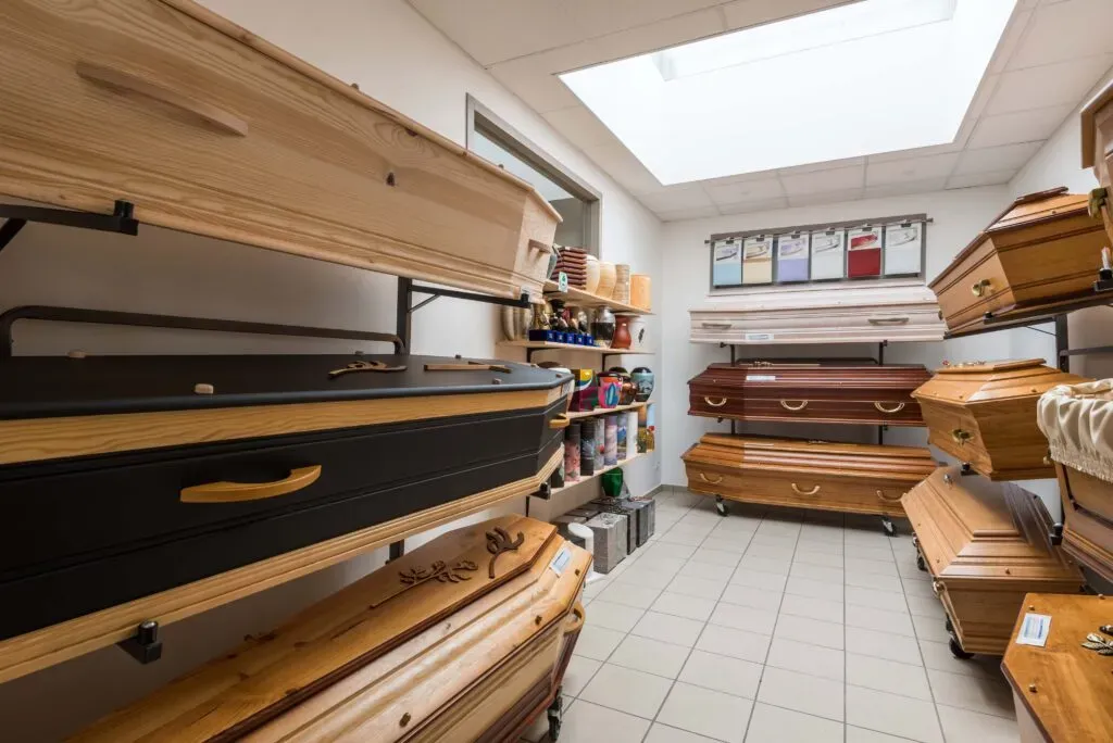 Salle d'exposition lumineuse avec une large sélection de cercueils en bois et d'urnes.