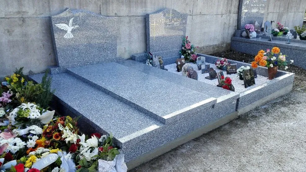 Monuments funéraires en granit gris ornés de plaques et fleurs au cimetière.