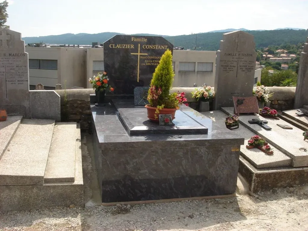 Caveau familial en granit foncé surmonté d'un arbuste et de plaques de souvenir.