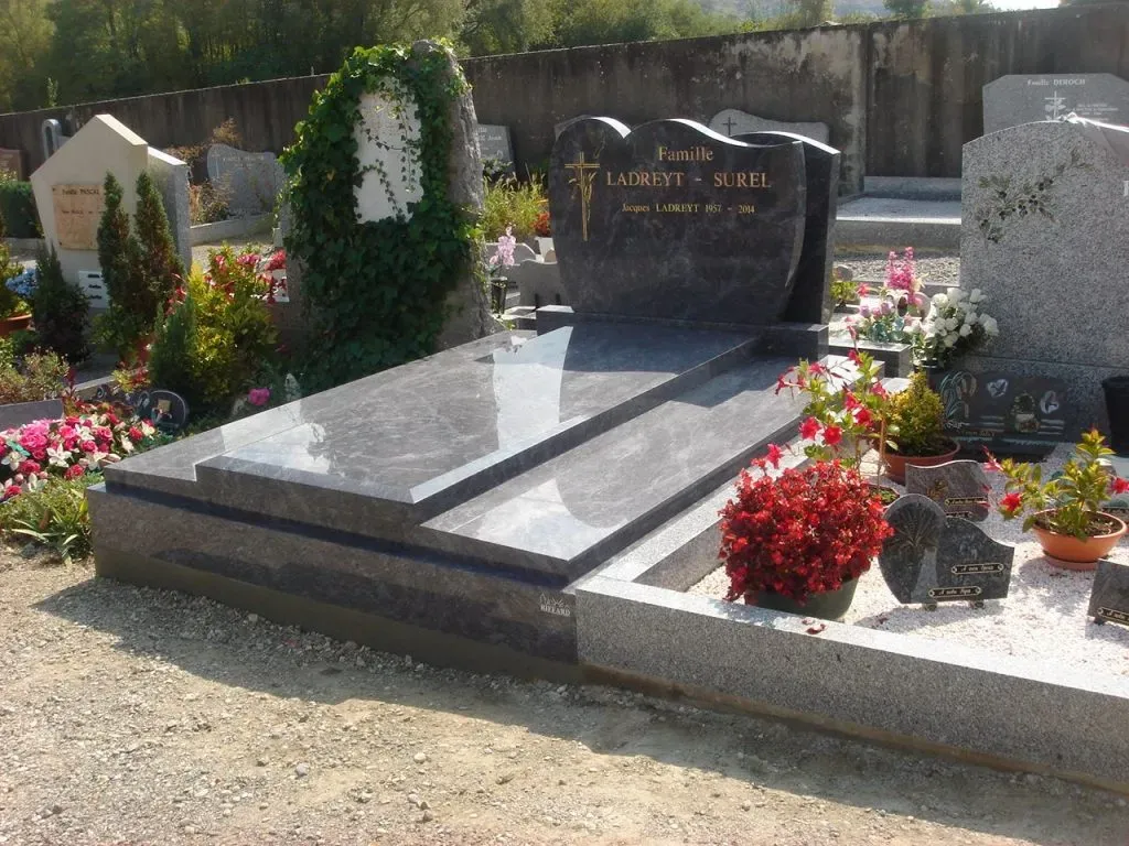 Monument funéraire en granit gris foncé avec stèle gravée et fleurs au cimetière.