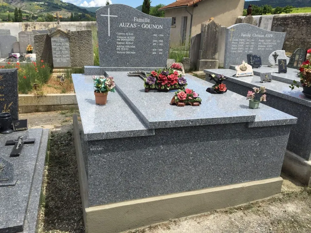 Tombe familiale en granit gris clair ornée de compositions florales colorées.